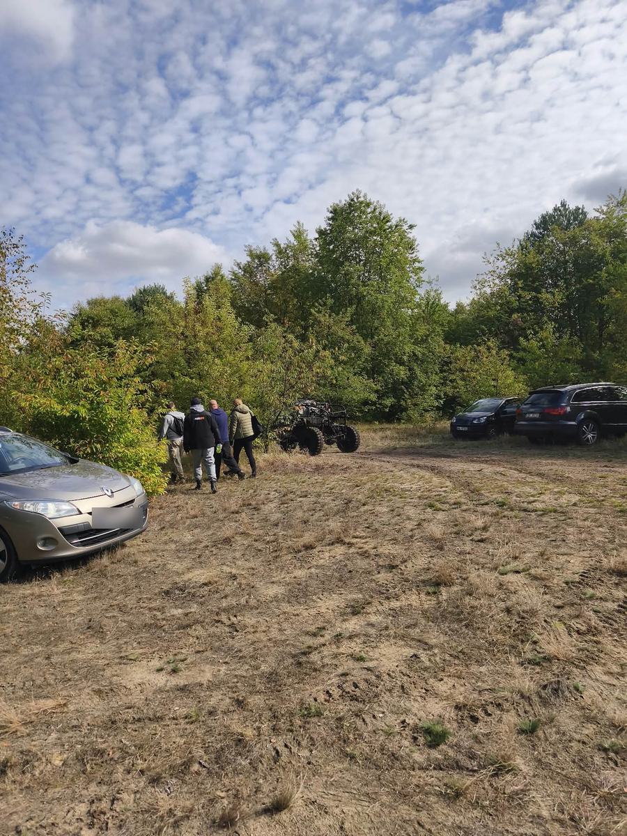 Parking przy terenie: auta osobowe, quad i grupa uczestników idących w stronę tras